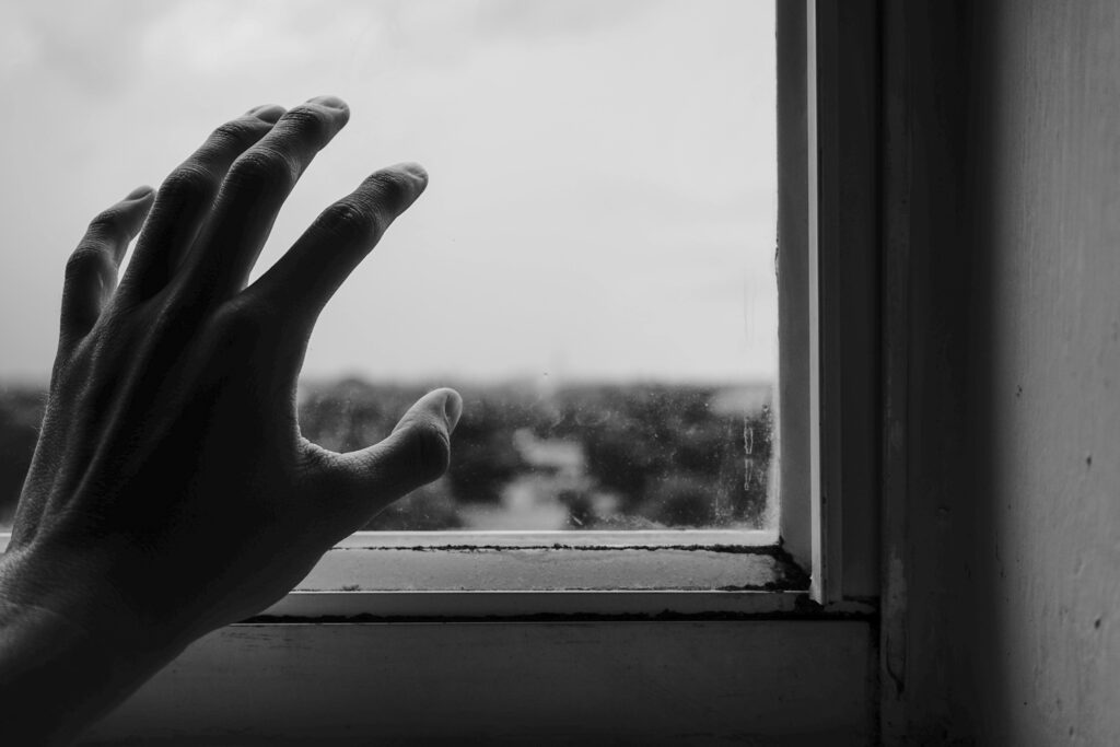 Otevření srdce – zkušenost klienta Abstract monochrome photo of a hand reaching towards a window, symbolizing longing.